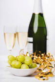 Mísa hroznů, láhev a sklenice šampaňského na stole