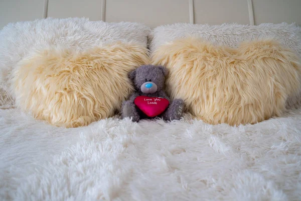 plush teddy bear on the bed near heart shaped fur pillows