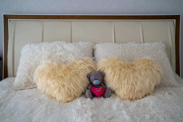 plush teddy bear on the bed near heart shaped fur pillows