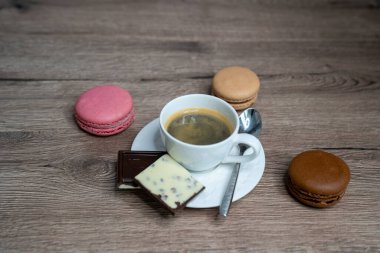 Beyaz fincanda kahve espresso, çay kaşığı ve ahşap arka planda kurabiye.