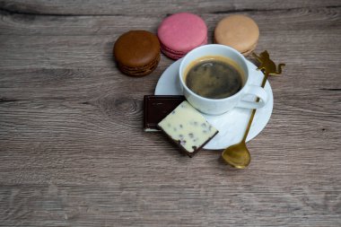 Beyaz fincanda kahve espresso, çay kaşığı ve ahşap arka planda kurabiye.