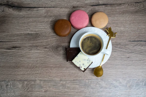 cup of coffee espresso in white cup and saucer, teaspoon and macaroons on wooden background