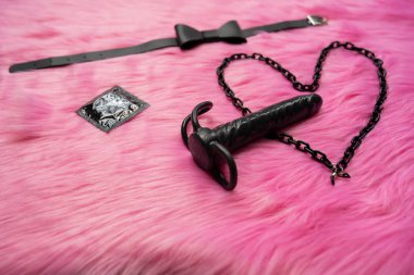Concept of safe sex and couple games.  Condom next to heart and butterfly tie and dark vibrator. Adult content of sex toys 
