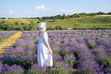 woman model in white dress outfit with hat is standing dancing in lavender field, photo session. Concept of freedom. Good picture for cover, calendar, postcard, wallpaper, background, product, website, blog, business, magazine, shop and store