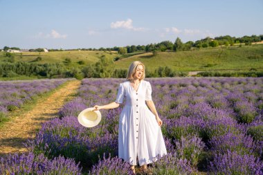 woman model in white dress outfit with hat is standing dancing in lavender field, photo session. Concept of freedom. Good picture for cover, calendar, postcard, wallpaper, background, product, website, blog, business, magazine, shop and store