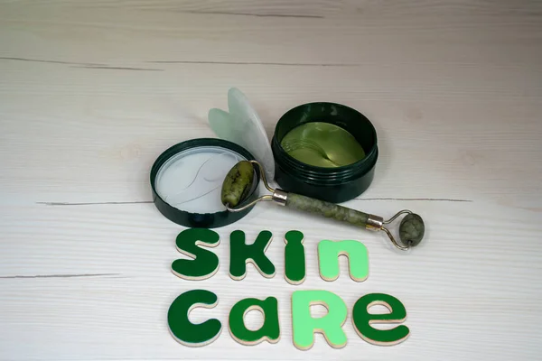 skin care accessories gua sha roller beauty tool, jade roller next to cream eye patches and word skin care made of letters, beauty salon concept