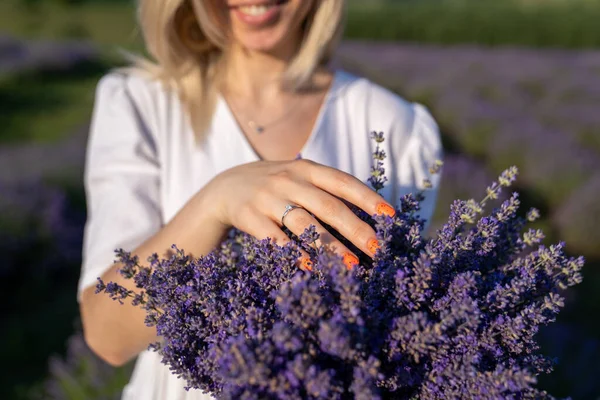close-up hands of a woman holding purple lavender flowers bouquet. young girl hand manicure with engagement diamond ring, on the background of a purple lavender field