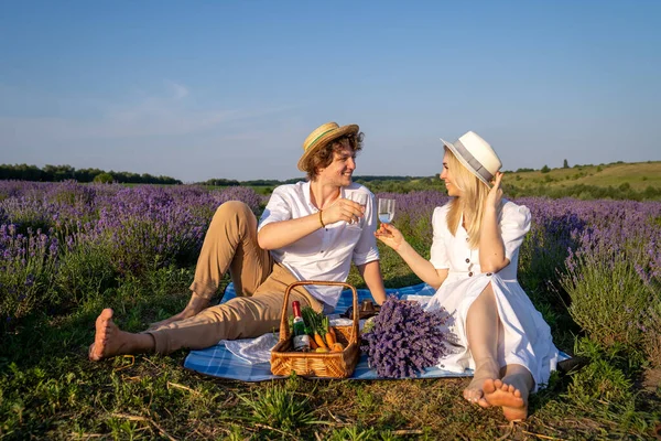 two persons couple in matching outfit have picnic in lavender field. They have fun, laugh and are feeding each other for photo session. Romantic relationship concept