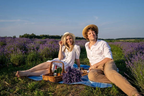 two persons couple in matching outfit have picnic in lavender field. They have fun, laugh and are feeding each other for photo session. Romantic relationship concept