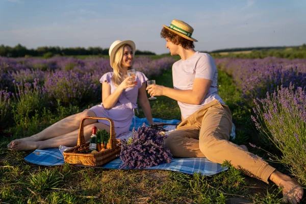 two persons couple in matching outfit have picnic in lavender field. They have fun, laugh and are feeding each other for photo session. Romantic relationship concept
