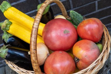 wicker wooden basket full of fresh ripe vegetables: tomato, cucumber, onion, zucchini, eggplant on brick background. Early harvest. Concept of healthy eating lifestyle diet nutrition. Consumer basket