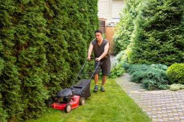 handsome man is cutting the lawn, process to cut the grass at the yard with special machine lawn mover, green garden