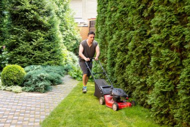 handsome man is cutting the lawn, process to cut the grass at the yard with special machine lawn mover, green garden