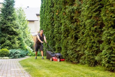 handsome man is cutting the lawn, process to cut the grass at the yard with special machine lawn mover, green garden