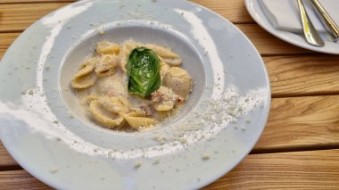 pasta with cheese and vegetables on a white plate at restaurant, eating out, way of serving food 