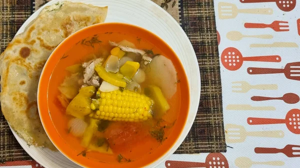 corn soup with vegetables and spices on a wooden table next to bread at kitchen