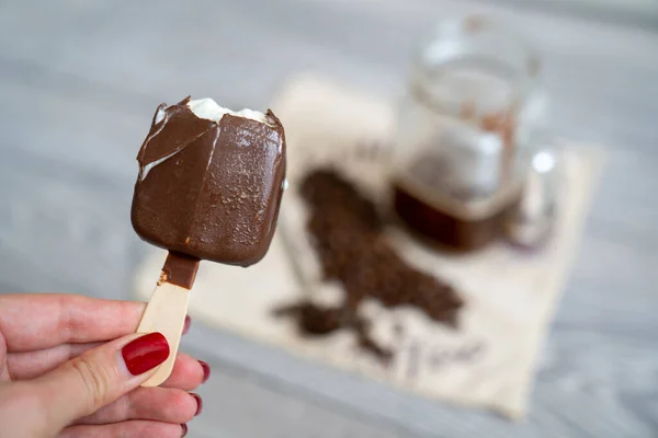 blur background, woman hand with manicure holds half eaten ice cream and pours it into strong black coffee espresso shot in glass cup, coffee set on table, long spoon and coffee beans on napkin, summer refreshment affogato