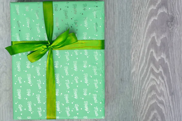 top view of green turquoise color gift box with green ribbon bow on grey wooden background. Concept: holiday, celebration, birthday, New Year, Christmas, Valentines Day, Mothers Day, Thanksgiving