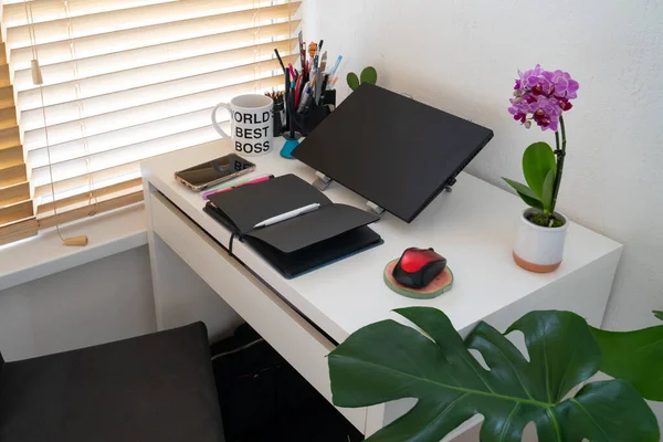 modern workplace: table desk with laptop, stationery, orchid plant, open white textbook with pen. Concept of work, work from home, study, back to school, home office