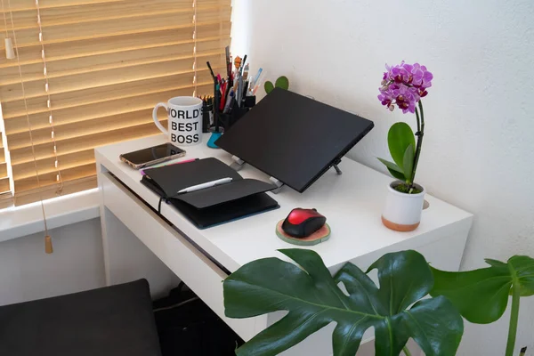 modern workplace: table desk with laptop, stationery, orchid plant, open white textbook with pen. Concept of work, work from home, study, back to school, home office