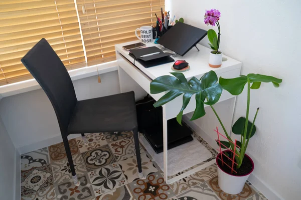 modern workplace: chair near table desk with laptop, stationery, orchid plant, open white textbook with pen. Concept of work, work from home, study, back to school, home office