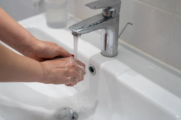 close up woman washing hands with soap and water, white foam, in the bathroom, under tap in the sink, personal hygiene and care, coronavirus prevention