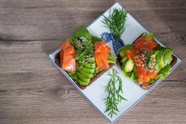 smoked salmon, avocado, dill, sesame seeds, arugula leaf green rocket on toast on white plate. Concept of healthy eating lifestyle diet nutrition. Omega 3 fatty acids source. Weight loss