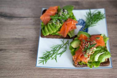 smoked salmon, avocado, dill, sesame seeds, arugula leaf green rocket on toast on white plate. Concept of healthy eating lifestyle diet nutrition. Omega 3 fatty acids source. Weight loss