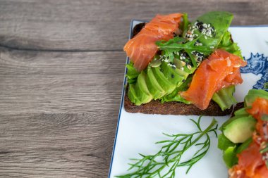 smoked salmon, avocado, dill, sesame seeds, arugula leaf green rocket on toast on white plate. Concept of healthy eating lifestyle diet nutrition. Omega 3 fatty acids source. Weight loss