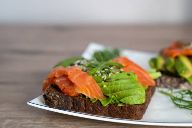 smoked salmon, avocado, dill, sesame seeds, arugula leaf green rocket on toast on white plate. Concept of healthy eating lifestyle diet nutrition. Omega 3 fatty acids source. Weight loss