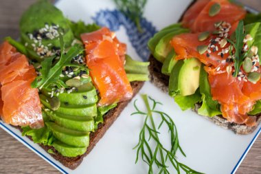 smoked salmon, avocado, dill, sesame seeds, arugula leaf green rocket on toast on white plate. Concept of healthy eating lifestyle diet nutrition. Omega 3 fatty acids source. Weight loss