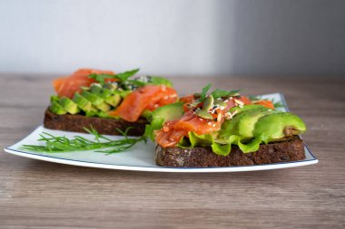 smoked salmon, avocado, dill, sesame seeds, arugula leaf green rocket on toast on white plate. Concept of healthy eating lifestyle diet nutrition. Omega 3 fatty acids source. Weight loss