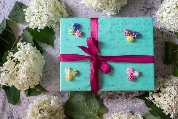 hydrangea flower, green turquoise color gift box with red ribbon bow on grey wooden background. Concept: holiday, celebration, birthday, New Year, Christmas, Valentines Day, Mothers Day, Thanksgiving