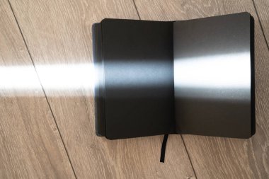 open text book on wooden background, black color of pages, creative effect lines of sun light sunbeam. Spell book of magic recipe, fairytale. Witch accessory for black magic. Process of reading