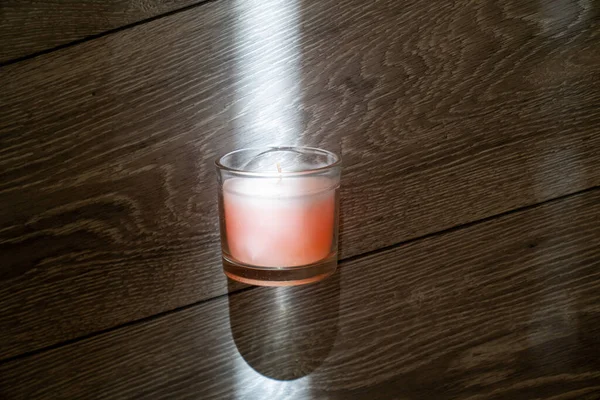 pink scented candle in a glass cover on a wooden background, sunbeam light creates creative effect of burning candle, therapy, meditation, aromatherapy to relax mindset, relive stress, smells good at home