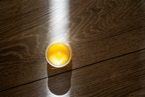 scented candle in a glass cover on a wooden background, sunbeam light creates creative effect of burning candle, therapy, meditation, aromatherapy to relax mindset, relive stress, smells good