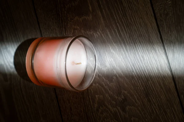 pink scented candle in a glass cover on a wooden background, sunbeam light creates creative effect of burning candle, therapy, meditation, aromatherapy to relax mindset, relive stress, smells good at home