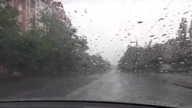 Kötü hava, yağmurlu gün, arabanın ön camına yağmur damlaları, ön cam silecekleri çalışıyor, yağmuru kaldırıyor, yolda çekim yapıyor, sokağa yağmur yağıyor.
