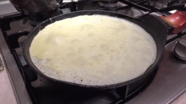 Büyükanne kadın modern mutfaktaki kızartma tavasında ince krepler pişiriyor.