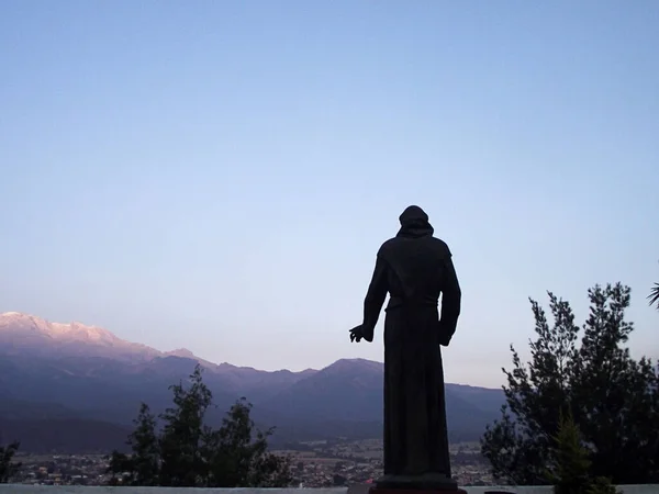 Arka planda dağ olan bir erkek keşiş heykeli silueti.
