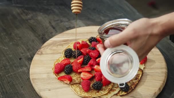 女人的手把蜂蜜倒在有草莓和黑莓的煎饼上 — 图库视频影像