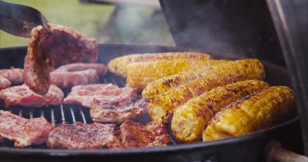边和香肠在火堆边的蒸肉烤肉上烤着甜玉米 朋友们正在后院的厨房里举行烧烤派对 一边吃着当地的健康食品 一边烤香肠 — 图库视频影像