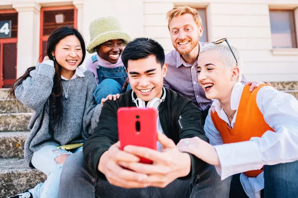 happy young group of smiling friends, having fun together using smartphones, man and women having fun together sitting in street with mobile phone. High Quality Photo