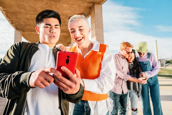 Two friends watching a video in a mobile phone. In the back three friends more browsing with a smartphone. high quality photo