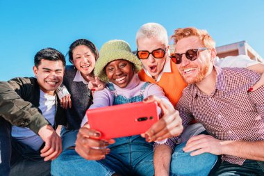 Five young multiethnic friends taking a selfie together outdoors under blue sky. High quality photo
