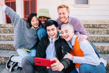Five diverse friends taking a picture with a smartphone smiling and having fun together sitting on the floor. high quality photo