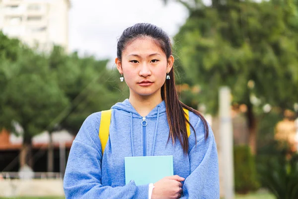 Portrait of serious teenager student standing at university campus looking at camera. Young chinese teen female at college. High quality 4k footage