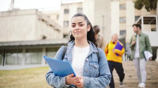 一个惊慌失措的女学生微笑着看着相机的近照 在背景下 一群青少年在大学校园里散步 教育概念 高质量的4K镜头 — 图库视频影像