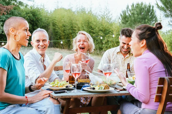 Group of adult multiethnic people laughing and having fun holding wine glasses at dinner party at the backyard. Lifestyle concept. High quality photo