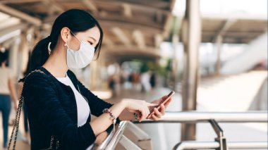 Genç yetişkin iş kadını Asyalı kadın virüs koronasını veya covid19 'u ve hava kirliliğini korumak için yüz maskesi takıyor. Cep telefonu uygulaması kullanılıyor. Gündüz konseptinde halk sağlığı ile kentsel yaşam tarzı.